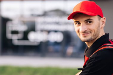 Kırmızı üniformalı bir adam sokakta dikiliyor ve yüzünü kameraya çeviriyor. Kırmızı sırt çantalı erkek kurye. Yeşil taşıma