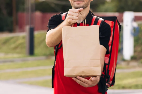 Food delivery man order from a restaurant. Handsome young man in a T-shirt and a cap. Happy delivery worker holding packet with food smiling. Delivery service door to door