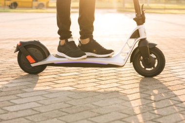 Siyah spor ayakkabılı genç hippi gün batımında elektrikli scooterla geziyor. Elektrikli scooter kullanan hippi bir adam. Çevre dostu ulaşım. Hızlı sürüş elektrikli taşıma