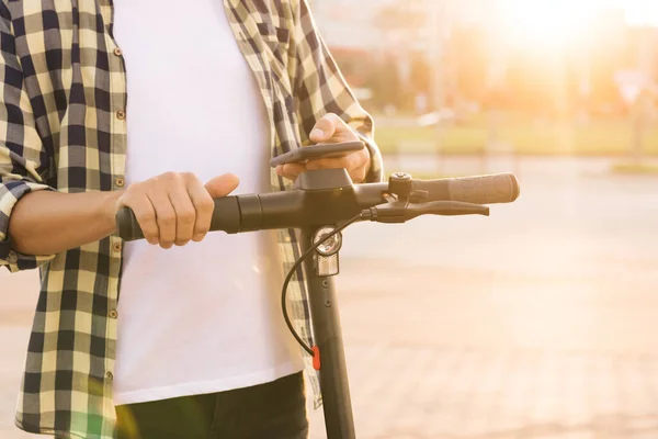 Kiralık adam, park yerinde elektrikli scooter ya da bisiklete biner, turist telefonu kullanırdı. Ekoloji taşımacılığı. Elektrikli scooter kullanan bir adam. E-scooter eko taşımacılığı — Stok fotoğraf
