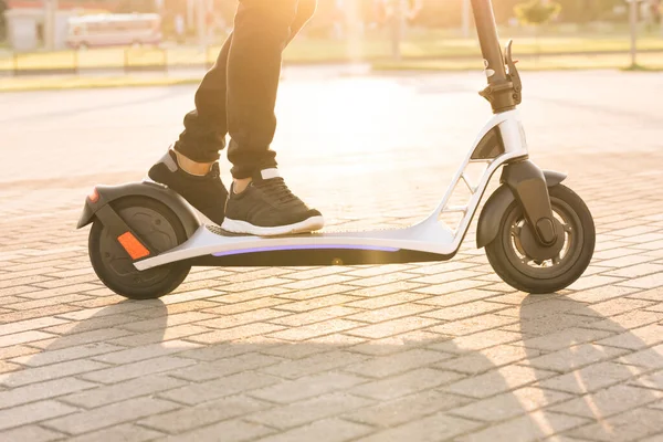 Transport ecologic. Transportul electric cu viteză rapidă. Omul hipster de echitatie un scuter electric. Împușcat pe picioare tânăr hipster om în adidași negri plimbare pe scuter mobil electric la răsăritul soarelui. — Fotografie, imagine de stoc