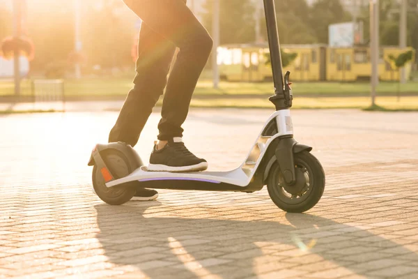 Modern yollarla işe giderken elektrikli scooter kullanan siyah ayakkabılı hippi bacaklar. Hızlı sürüşlü elektrikli taşıma. E-scooter sürücüsü, insan sürüşü paylaşımı veya kişisel çevre taşımacılığı