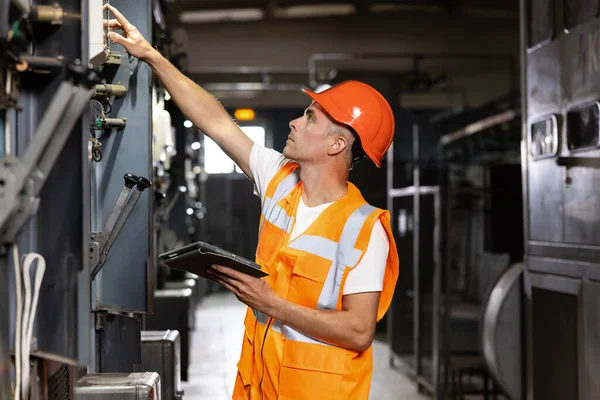 Ingeniero que utiliza la comprobación y la inspección digitales de la tableta en el panel del MDB que trabaja con el tablero eléctrico para comprobar la gama del funcionamiento del voltaje en la fábrica principal de los tableros de distribución —  Fotos de Stock