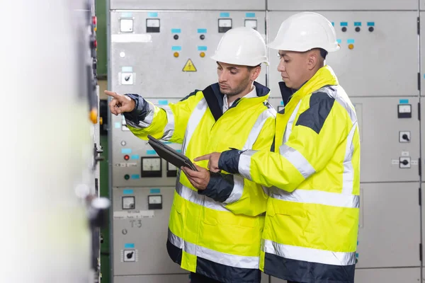 Elektrik mühendisleri kontrol panelini tabletle kontrol ediyorlar. Yüksek voltajlı elektrik santrali. Elektrik mühendisleri güneş panelinin terminal kutusunun yanında duruyorlar.