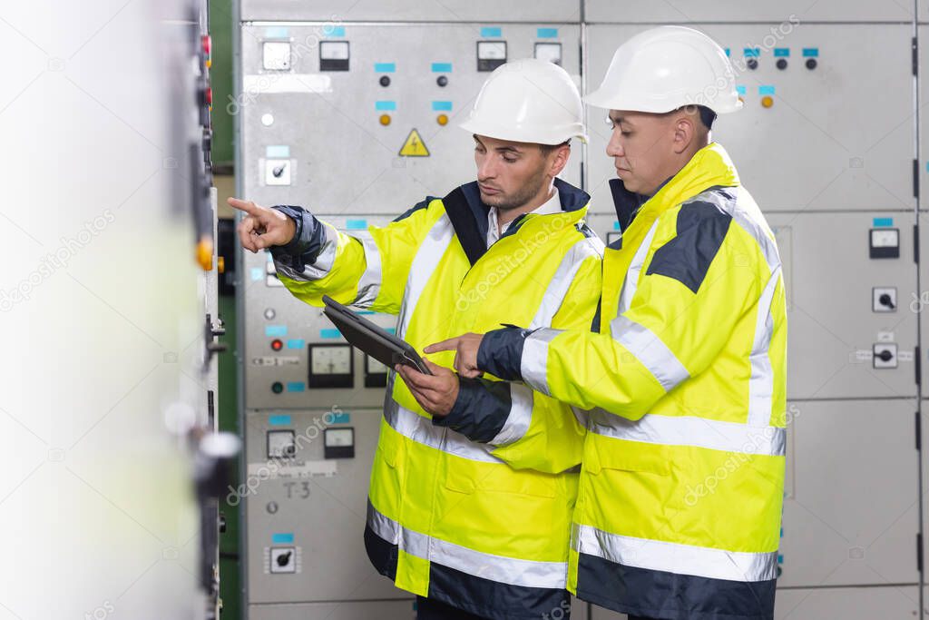 Electrical engineers checking control panel board with tablet. High voltage power station. Electrical engineers standing near therminal box of solar panel