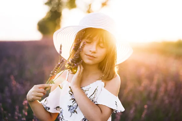Zamknij portret młodej szczęśliwej dziewczynki z kapeluszem na głowie na polach lawendy na tle. Kid girl ubrana w kapelusz na wiosnę — Zdjęcie stockowe