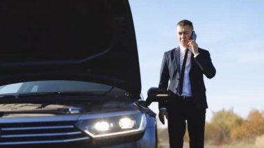 Hayal kırıklığına uğramış iş adamı telefonda konuşuyor. Ayrıca kaputu açık kırık bir araba. Çaresiz adamın yardıma ve yardıma ihtiyacı var. Elektrikli araba kazası. Araba arızası. Arabanın dışındaki genç adam..