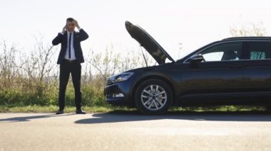 Siyah takım elbiseli, kaputu açık, bozuk bir arabanın yanında duran ve cep telefonuyla konuşan olgun bir iş adamı. Yoldaki sorunlar sırasında erkek sürücü yardım için birilerini arıyor. Araba kazası. Araba sorunu.