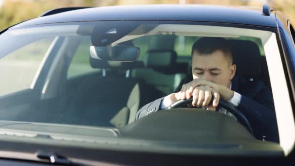 Conducteur mâle épuisé tenant la tête dans le volant tout en étant assis dans une voiture de luxe moderne latérale. Homme d'affaires caucasien en tenue formelle prenant arrêt sur la route après une longue équitation — Video