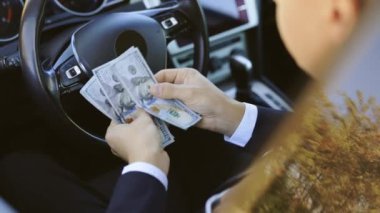 Para sayan işadamı lüks arabanın içinde ödeme günü ödüyor. Farklı mezheplerin dolarları. Başarılı iş adamı zaferi kutluyor. Nakit parayı araçta tutuyor.