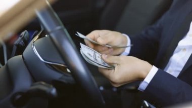 Arabada oturmuş dolarları sayan bir adam. Erkek eli kapalı para saymak. Kazanç ya da rüşvet kavramı, sigorta ya da kredi, yatırım. Lüks arabada para sayan bir adam.