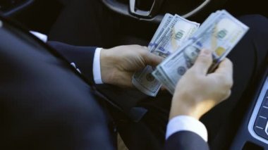 Başarılı bir iş adamı zaferi kutluyor. Nakit parayı araçta tutuyor. Farklı mezheplerin dolarları. Lüks bir arabada oturan adam dolarları sayıyor..