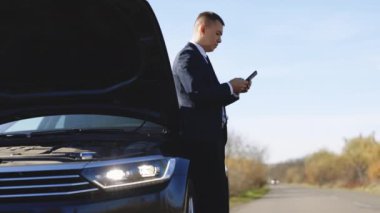 Kırsal kesimde yaşayan üzgün işadamının portresi, akıllı telefonu kullanarak tahliye ediciyi çağırıyor. Erkek adam akıllı telefonunu kullanıyor çünkü elektrikli arabası bozuk.