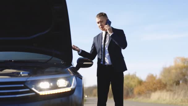 Hombre hablando por teléfono y mirando el motor de los coches. joven uso de teléfono inteligente, stading en la carretera cerca del coche roto abrió la capucha, llamando a los servicios de asistencia del coche, ayudar a reparar. — Vídeos de Stock