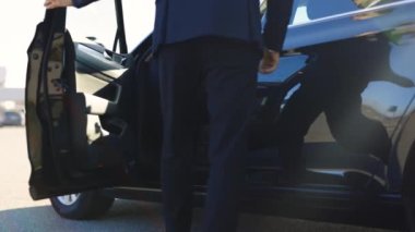 Başarılı takım elbiseli işadamı, siyah lüks elektrikli arabasına doğru yürür ve kulübesine girer. İş elbiseli bir işadamı park halindeki arabaya doğru yürür. Adam arabasına biniyor ve sürmeye hazırlanıyor.