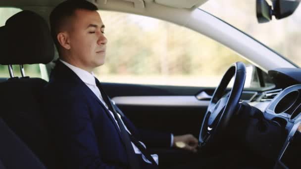 Портрет мужчины-бизнесмена, сидящего за рулем автомобиля. Молодой веселый мужчина сидит в современном роскошном автомобиле, останавливаясь в центре города — стоковое видео