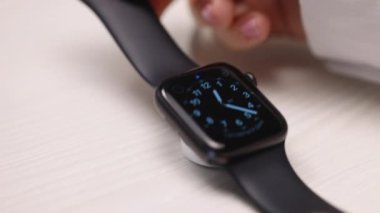 Akıllı saat beyaz arka planda kablosuz şarj cihazına şarj oluyor. QI kablosuz şarj. Dokunmatik ekran akıllı seğirmesi manyetik kablosuz prizde şarj oluyor..