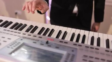 Piyanist konserde sahnede güzel bir sentezleyicide çalar. Müzisyen konser sahnesinde bir müzik aleti çalar. Sentezleyici. Erkek eller piyano çalıyor. Adam tuşlardaki parmaklara dokunur.