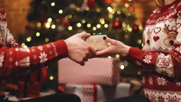 女性の手に緑の弓でクリスマス包装紙にプレゼントを与える男性の手。緑色のリボンで結ばれた箱を持っている人。家族の休日、クリスマス、新年、お祝いの概念 — ストック動画