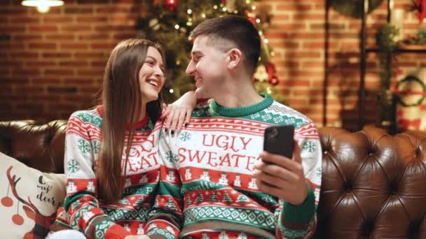 Attrayant homme et femme Parler par appel vidéo Envoyer des émotions positives en regardant la caméra. Joyeux couple assis à la maison tout en enregistrant les voeux de Noël. Bonne année. Joyeux Noël. — Video