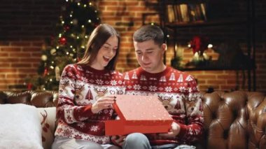 Kadın hediye kutusunu açtıktan sonra şaşırdı ve heyecanlandı. Mutlu adam sevgilisine Noel hediyesi hazırlıyor. Tatil kavramı, romantizm, sürpriz. Tatil mucizesi