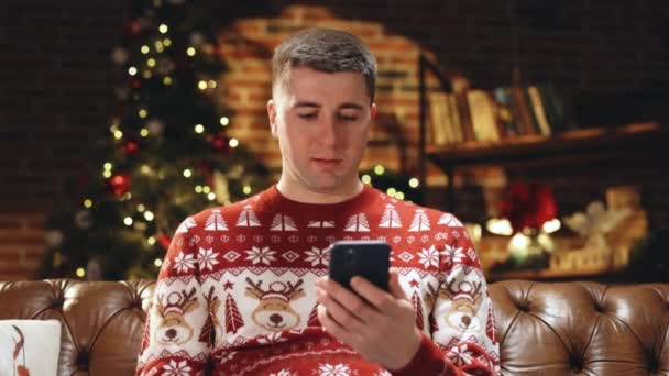 Portrait d'un jeune homme caucasien joyeux souriant avec un visage surpris tapotant sur un téléphone intelligent cellulaire se sentant excité et heureux de gagner à la loterie de Noël. Joyeux Noël Noel concept. Miracle de vacances — Video