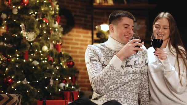 Neşeli insanlar yılbaşı ve yeni yıl kutlamaları için kadehlere şarap dolduruyorlar. Mutlu çift kadehleri tokuşturur ve birlikte yeni yılı kutlayalım. 2022 'de evde parlayan Noel ağacının yanında. — Stok video