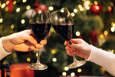Parlayan çelenkle süslenmiş Noel ağacına karşı şarap kadehleriyle tezahürat eden bilinmeyen insanların ellerini kapatın. Arka plan bulanık, Bokeh. Mutlu yıllar.