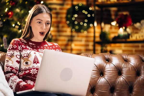 Young pretty cheerful happy girl look laptop xmas win inside home. Woman sitting on sofa with laptop celebrating victory with christmas decorations indoors. Screaming for success. Celebration concept — Stock Photo, Image