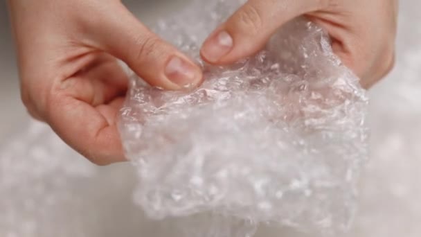 Female hands burst air bubbles on bubble wrap on a white background. Popping bubble wrap. Calming the nervous system concept – Stock-video