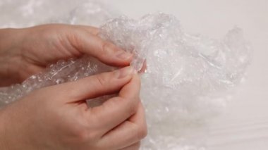 Masada otururken kendini sakinleştirmek için baloncuklu naylon çalan tanınmayan genç kadının yakın çekim elleri. Evde plastik baloncuklu ambalaj yapan kadınların yakın çekimi