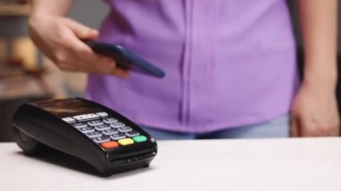 Akıllı telefondan yapılan temassız ödeme. Kablosuz ödeme konsepti. Banka terminalinde siparişi ödemek için akıllı telefonlu, nakitsiz cüzdan kullanan beyaz bir kadının yakın çekimi. NFC ödemeli akıllı telefon.