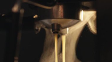 Making a cup of strong coffee in a coffee machine, the back light illuminates the steam. Pouring coffee stream from professional machine in cup. Making double espresso. Flowing fresh ground coffee