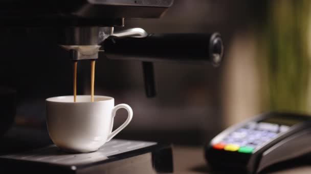 Espresso machine making fresh coffee. Pouring coffee stream from machine in cup. Espresso in a white cup. Tasty coffee. Caffeine. Coffeeshop in the background with credit card machine terminal NFC — Vídeo de Stock