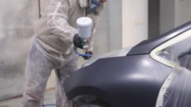 Erkek teknisyen araba parçalarını boyuyor. Endüstriyel sprey boya işlemi. Otomobil boyacısı özel bölmedeki araba kanadına siyah boya püskürtüyor. Araç parçaları araba servisi atölyesinde boyanıyor