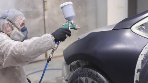 Mästaren målar en del av bilen i bilservice. Han använder besprutningsmaskin, håller den i handen, klädd i skyddande uniform. Modern bilmålning. — Stockvideo