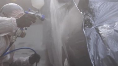 Ressam arabayı garajda boyar. Profesyonel sprey silahla araba boyama. Usta araba servisinde otomobilin bir parçasını boyuyor. Endüstriyel sprey boya işlemi
