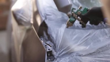 Endüstriyel sprey boya işlemi. Otomobil boyacısı özel bölmedeki araba kanadına siyah boya püskürtüyor. Araba servisi atölyesinde araç parçaları boyuyorum. Erkek teknisyen araba parçalarını boyuyor.