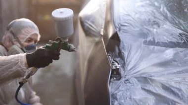 Erkek teknisyen araba parçalarını boyuyor. Endüstriyel sprey boya işlemi. Profesyonel araba boyacısı bir kaporta boyuyor. Adam Sprey Silahla Parça Boyar