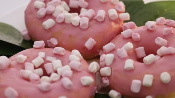Primer plano de unas deliciosas rosquillas redondas cubiertas de glaseado dulce gira sobre un fondo brillante. Dulce postre rosado donas — Vídeo de stock