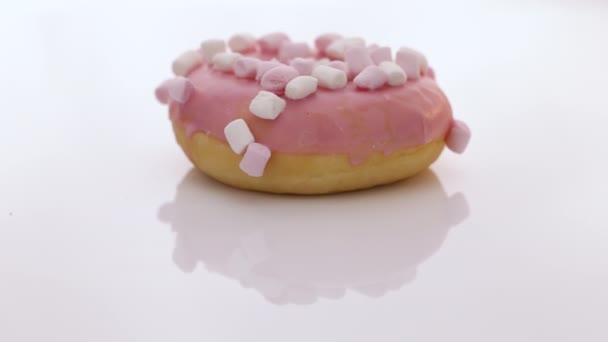 Вращающийся крупным планом снимок розового вкусного сладкого пончика с красочными брызгами на белом фоне. Вкусный вращающийся пончик на белом фоне. Десерт. Цветной розовый пончик — стоковое видео