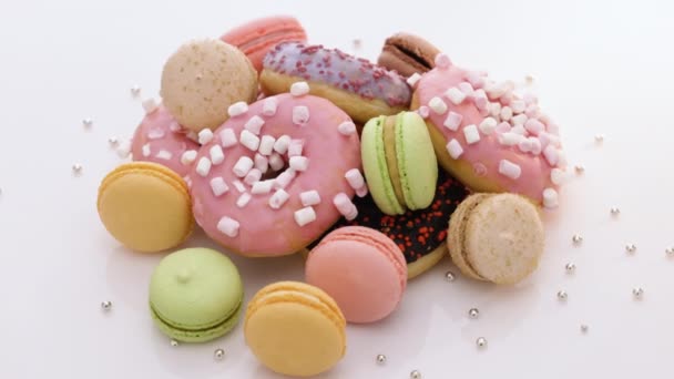 Macaroons and donuts rotate on a white background. Macaroons, sweets are spinning. Many multi-colored macaroons donuts with different tastes, dessert — Stock Video