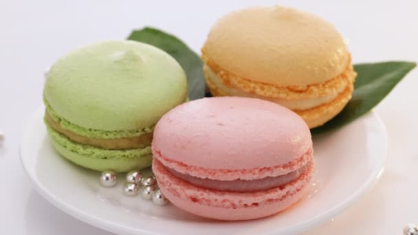 Primer plano de macarrones multicolores, macarrones franceses, pastelería codiciosa. Dulces de postre francés galletas de macarrones de colores dispuestos en un plato de tiempo girando sobre fondo blanco — Vídeos de Stock