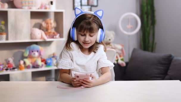 Feliz niña adolescente caucásica sosteniendo el teléfono celular usando el dispositivo de teléfono inteligente en casa. Joven blogger sonriente suscribiéndose a nuevas redes sociales, comprando en internet, ordenando productos en línea en aplicaciones — Vídeo de stock