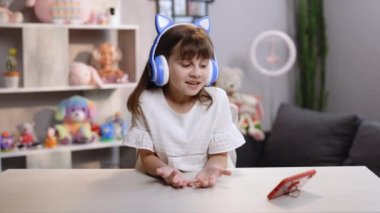 Küçük beyaz kız vlogger kameraya el sallayarak sosyal medya blogu için video blogu kaydediyor, sanal arkadaş arıyor ve online toplantı yapıyor.