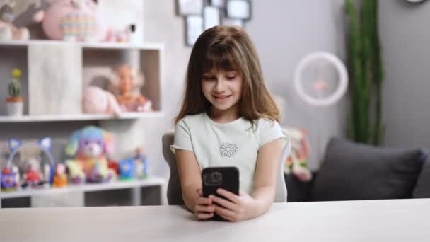 Retrato lindo pequeño caucásico niña saludando de la mano mirando a la webcam hablando con la cámara usando el teléfono inteligente sentarse en la mesa de video conferencia de llamadas en la reunión de chat virtual con el amigo de distancia social — Vídeos de Stock