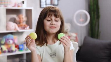 Genç esmer kız doğru kararı veremiyor ve önce hangi makaronu ısıracağını seçemiyor - limon ve bereyle doldurulmuş mu yoksa fıstıklı krema ile sağdan soldan yeşile boyanmış mı?