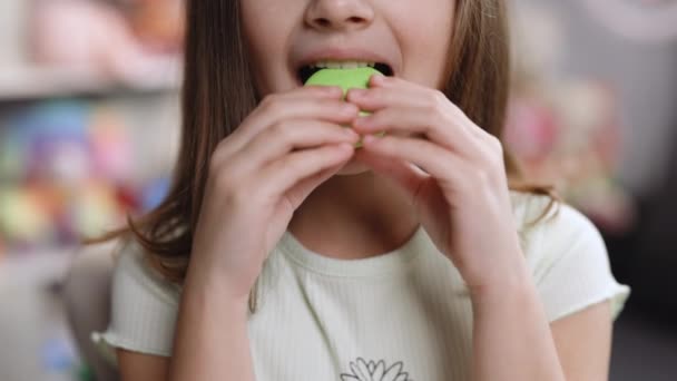 Zavřít přední pohled, nepoznatelné dítě brunetka dívka s velkým úsměvem a bílé zdravé zuby kousne pistácie macaron cookie. Chutné sladké barvy macaron — Stock video