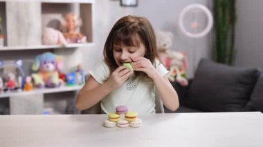 Çekici burunlu kız bir badem kurabiyesini ısırıyor, zevkine şaşırıyor, neşeyle gülümsüyor ve parmağını kaldırıyor. Pozitif duygular, gurme olmak, tatlıya düşkün olmak, lezzetli. Ev arka planında kadın portresi