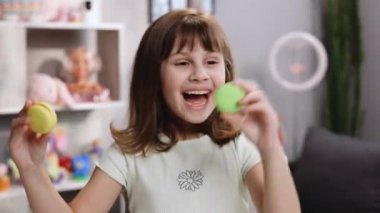 Genç kız tatlı kurabiyeleriyle oynuyor, kurabiyeleri gözünün etrafına bardaklar gibi tutuyor. Renkli bir ev arka planında gözlerini kurabiyelerle kapayan küçük bir kızın gülen yüzü. Mutlu olmak.